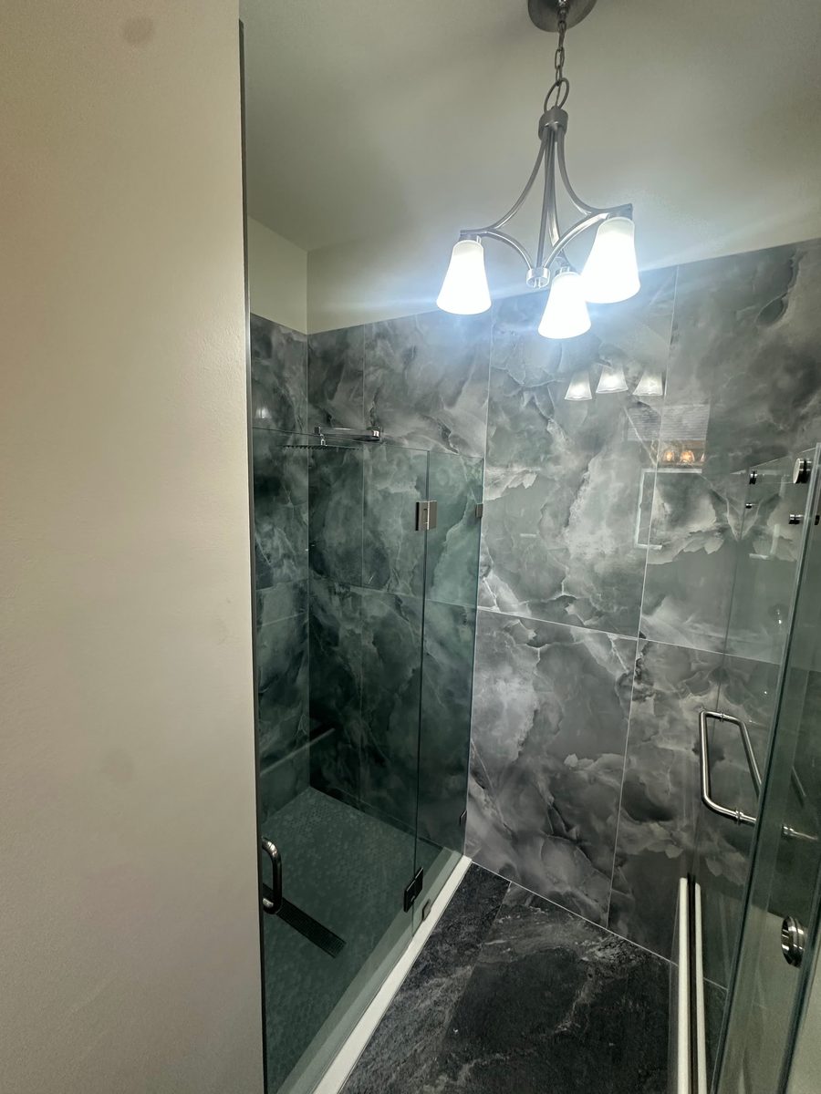 Walk-in shower with dark marble-look tile and frameless glass door