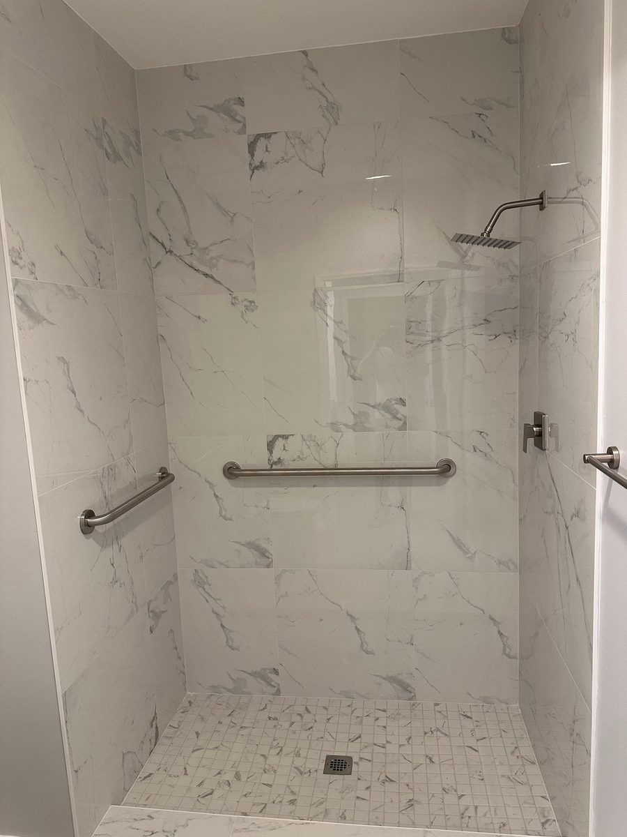 White marble-look tile shower with rain head and grab bars
