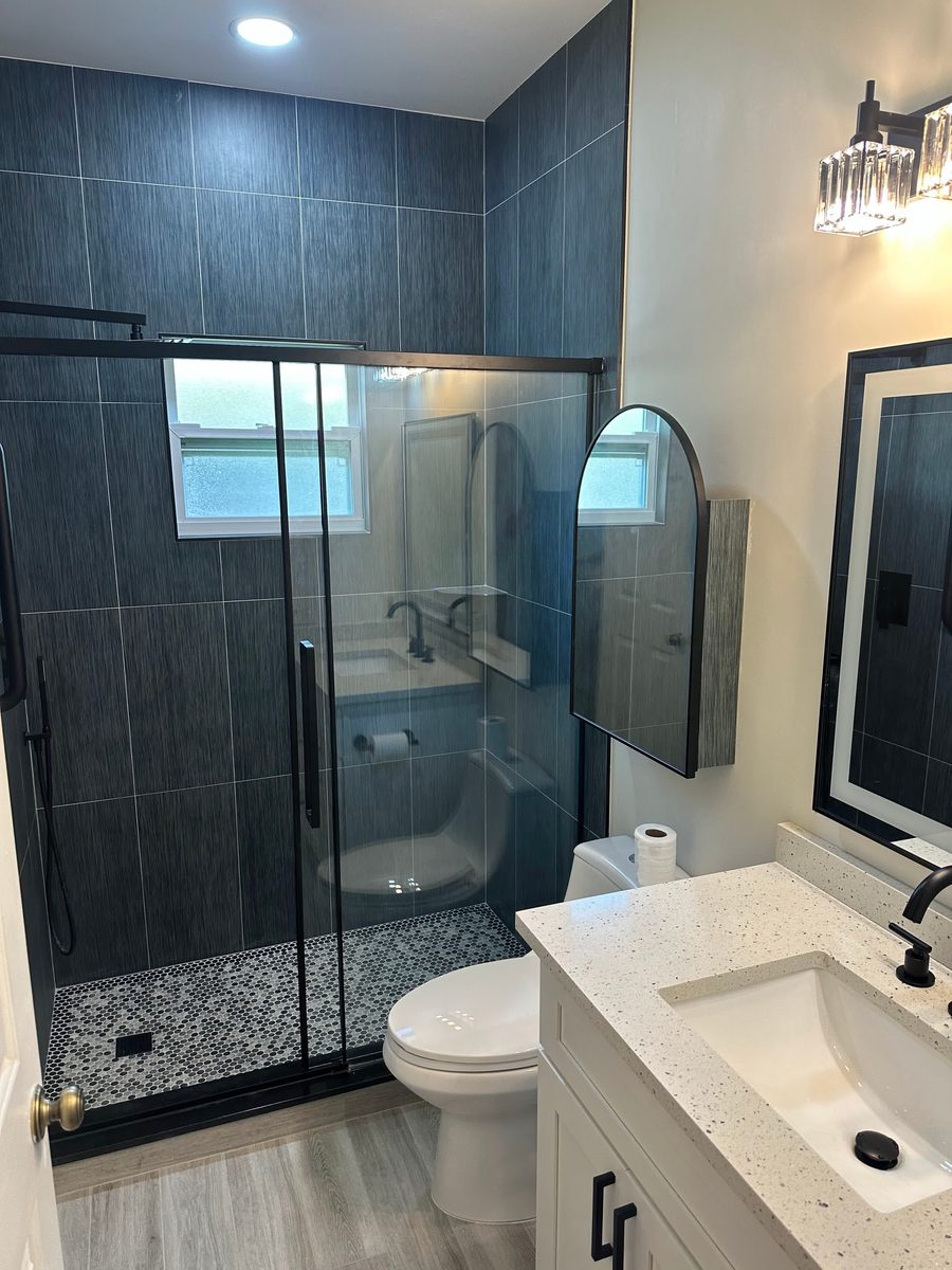 Navy tile shower with glass door beside a quartz vanity