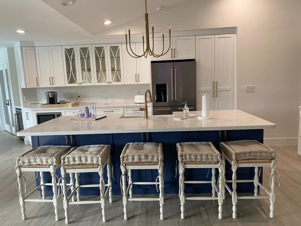 Navy kitchen island with brass chandelier and upholstered stools
