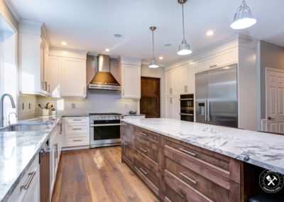Luxury home interior boasts amazing white kitchen with custom white shaker cabinets, endless marble topped kitchen island with drawers and stainless steel appliances over wide planked hardwood floor in Vero Beach FL